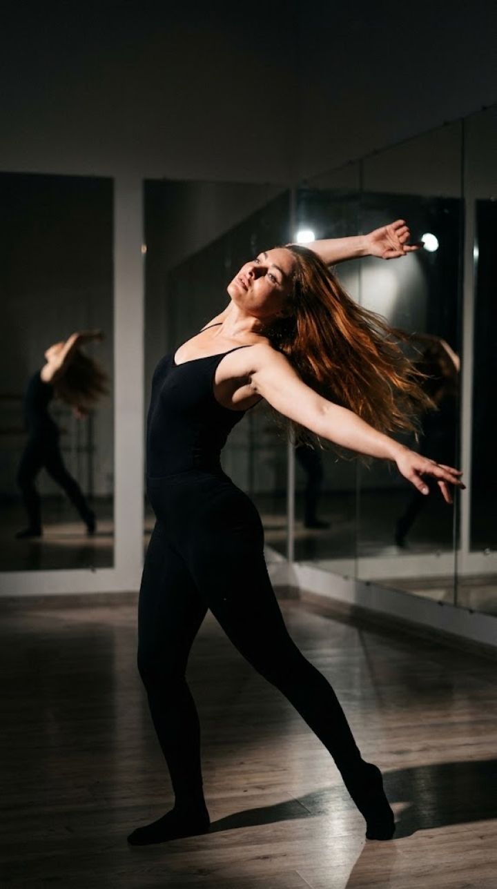 Vertical frame: dance pose with a turn, back arched, arms extended, studio with mirrors, dramatic...