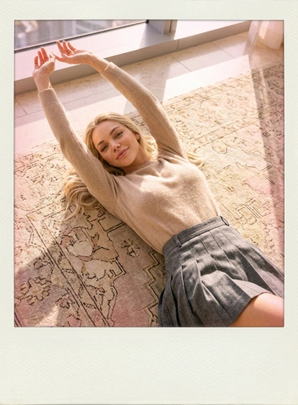 Donna Rilassata su Tappeto Soleggiato con Braccia in Alto, Maglione Cashmere e Gonna Plissettata Alta - Stile Polaroi...