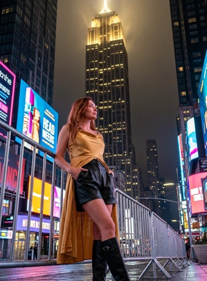 Foto Ultra-Realiste: Grua në Veshje të Artë Saten pranë Empire State Building Natën me Ndriçim Dramatik