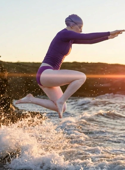 Lompatan Dinamis Penuh Tubuh dari Tepi Tebing Saat Sunset Golden Hour, Rash Vest Ungu dan Bikini