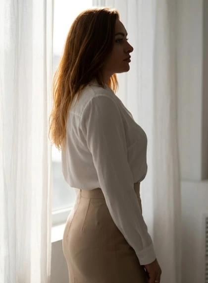 Potret Siluet Wanita Dekat Jendela dengan Efek Halo Backlight Lembut, Rok Pensil Beige High-Waisted dan Blus Putih