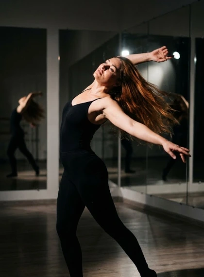 Vertical frame: dance pose with a turn, back arched, arms extended, studio with mirrors, dramatic spot light, shadows...