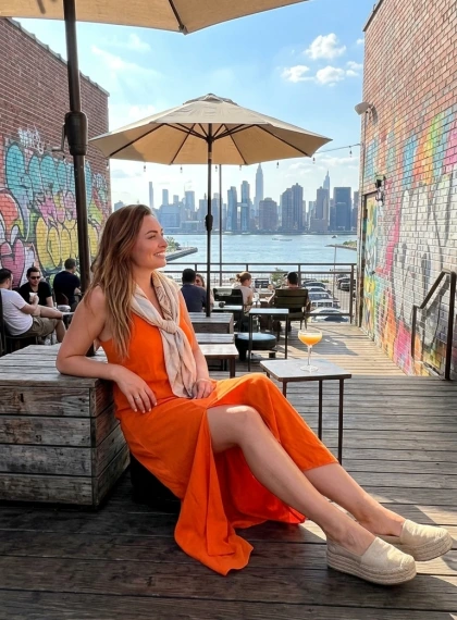 Žena v oranžových maxi šatech na terase v Williamsburgu s výhledem na East River