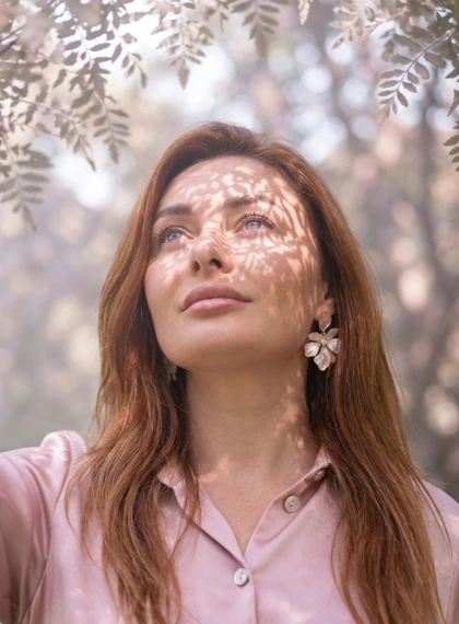 सपनीला सिनेमाई क्लोज़-अप पोर्ट्रेट: झुका सिर, ऊपर की ओर आँखें, वन प्रकाश और कोहरे वाली पृष्ठभूमि